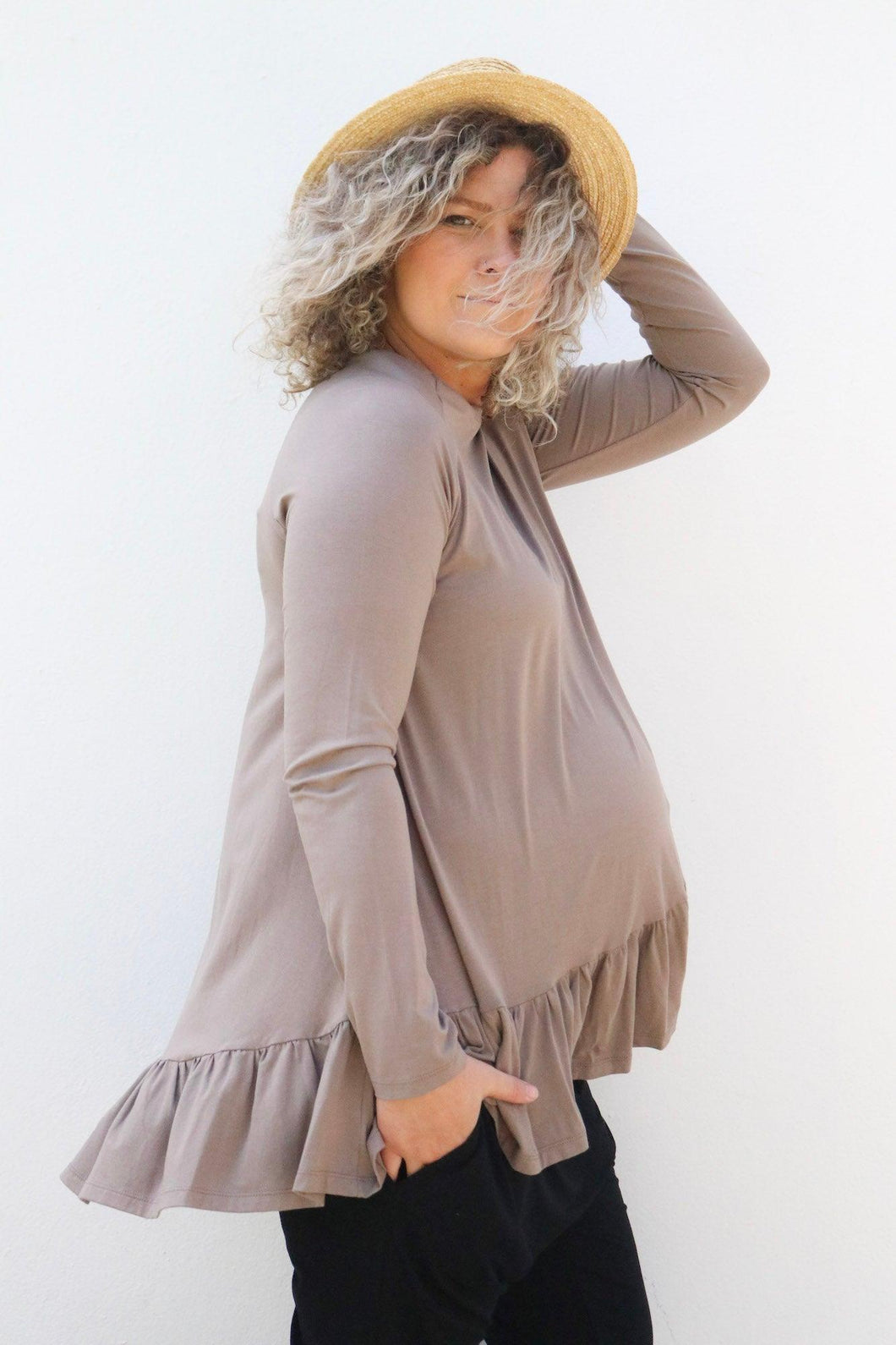 Pregnant mum standing side on wearing a hat and brown long sleeve top with her hand in her pocket
