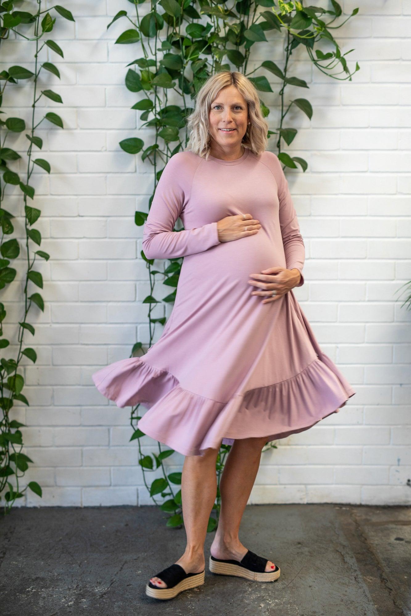 pregnant lady standing infront of an indoor plant twirling in a pink long sleeve dress