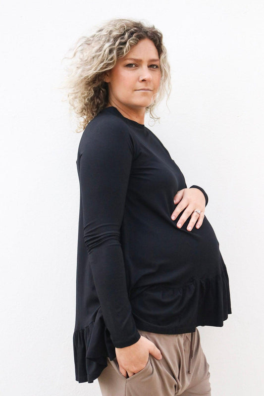 side view of a pregnant lady in a black long sleeve top holding her baby bump