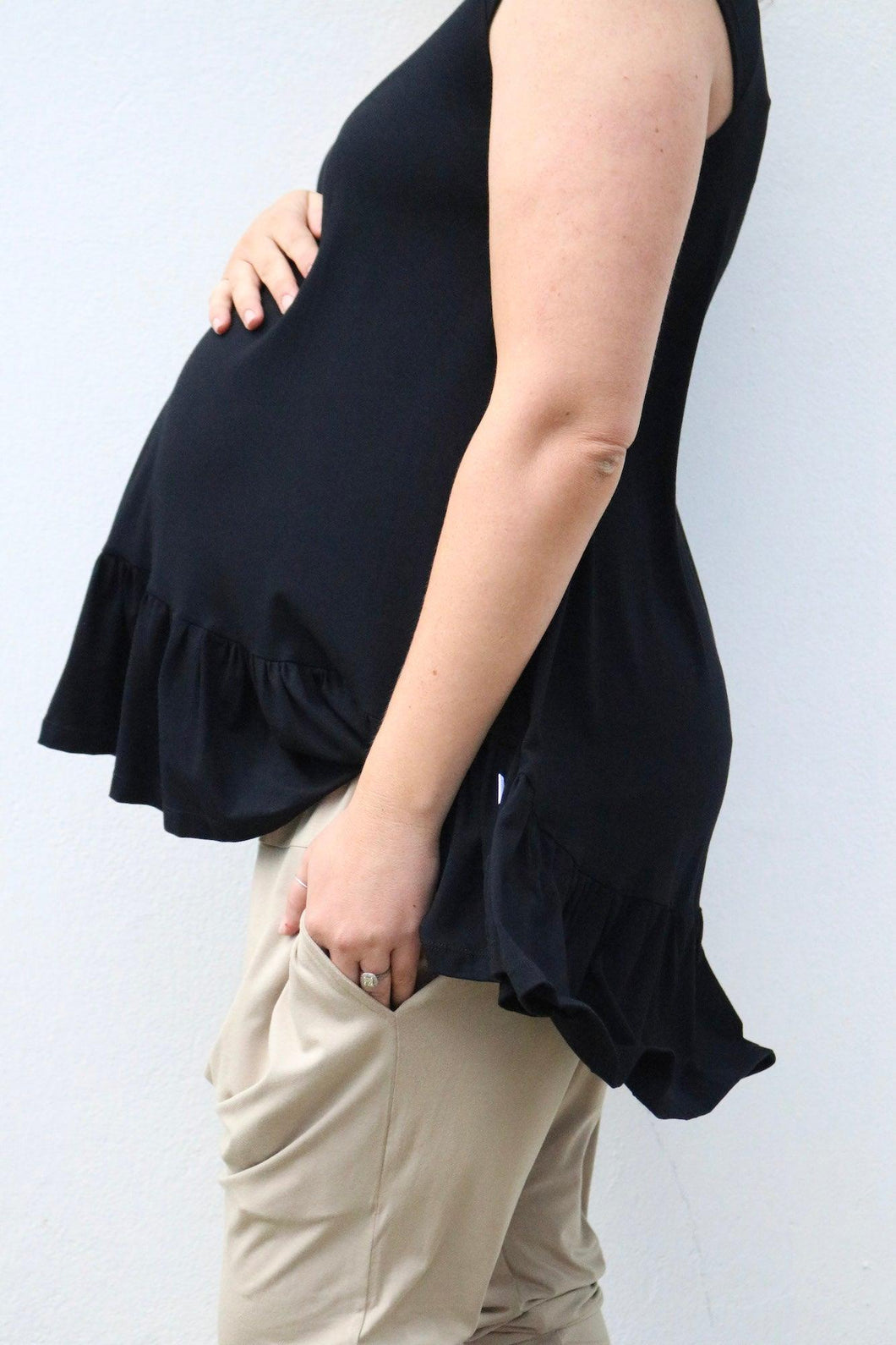 Side on view of a baby bump in a black short sleeve top and neutral pants